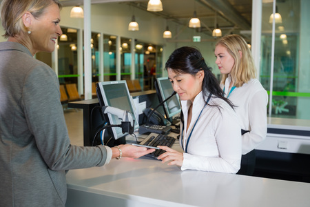 Businesswoman Showing Smart Phone To Receptionist At Airport Couの写真素材