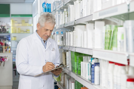 Chemist Writing On Clipboard While Standing By Shelvesの写真素材