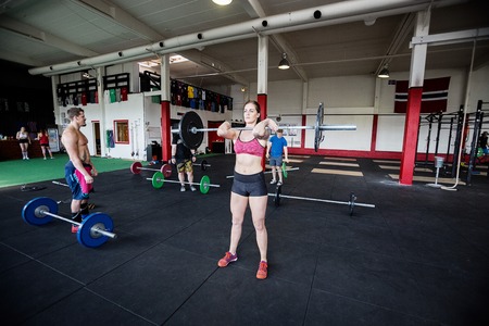Woman Lifting Barbell While Man Standing In Gym