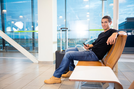 Young Man With Mobile Phone And Laptop At Airportの写真素材