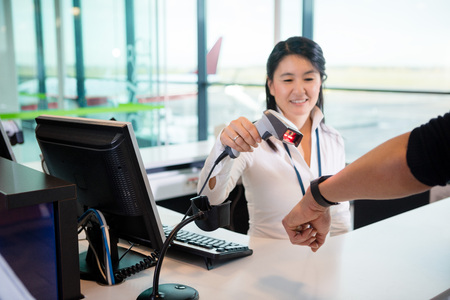 Smiling Receptionist Scanning Smart Watch Of Passenger At Airporの写真素材