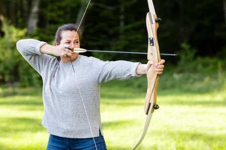 Female Archer Aiming With Bow And Arrow In Forestの写真素材