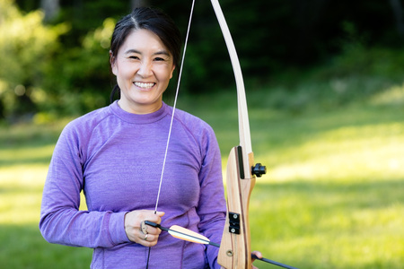 Smiling Mature Athlete Holding Bow And Arrow In Forestの写真素材