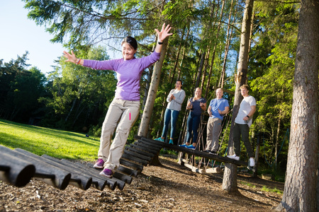 Friends Motivating Woman Crossing Log Bridge In Forestの写真素材
