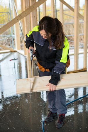 Full Length Of Female Carpenter Cutting Wood With Hand Sawの写真素材