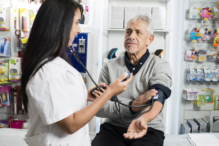 Female Chemist Checking Blood Pressure Of Senior Manの写真素材