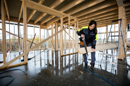 Female Carpenter Cutting Wood With Hand Saw In Incomplete Buildiの写真素材