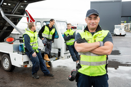 Mature Worker Standing Arms Crossed While Colleagues chattingの写真素材