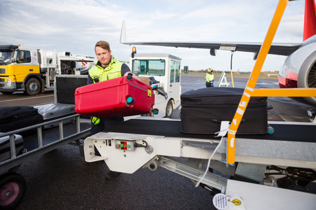 Worker Unloading Luggage From Conveyor Attached To Airplaneの写真素材