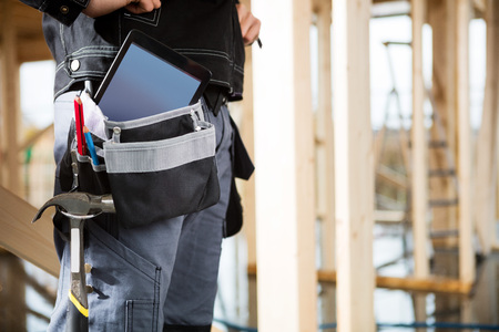 Young Carpenter With Tablet Computer And Tools In Bag At Siteの写真素材