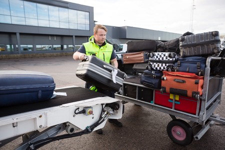 Worker Stacking Luggage On Trailer From Conveyor On Runwayの写真素材