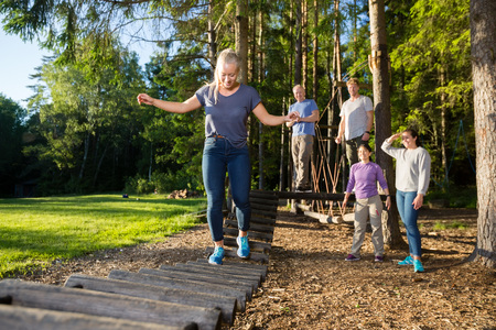 Friends Watching Woman Crossing Log Bridge In Forestの写真素材
