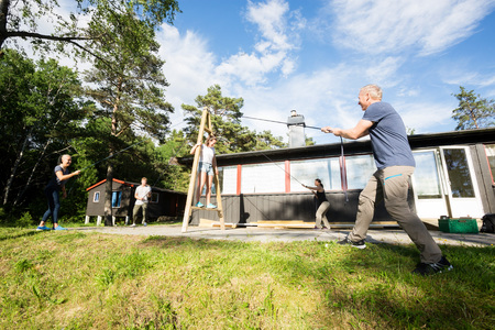 Friends Pulling Ropes To Balance Woman On Structure Outside Cottの写真素材