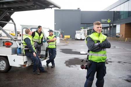 Confident Worker Standing Arms Crossed While Colleagues Communicの写真素材