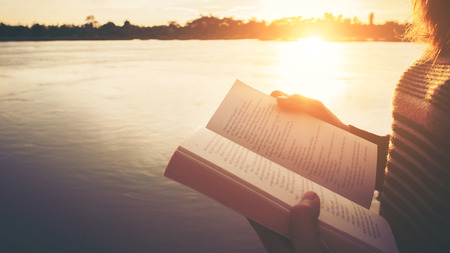Close up hand of young woman reading the book at riverside in the evening.の写真素材