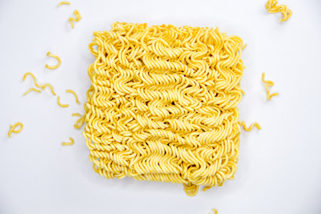 uncooked instant noodles with pieces of instant noodles around, texture of dry instant noodles on white backgroundの写真素材