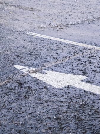 Close-up of heavy rain falling on asphalt road with white traffic arrow sign.の写真素材