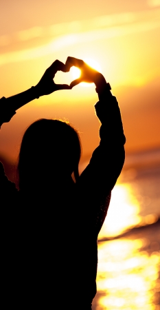 women silhouette makes heart shape sunsetの写真素材