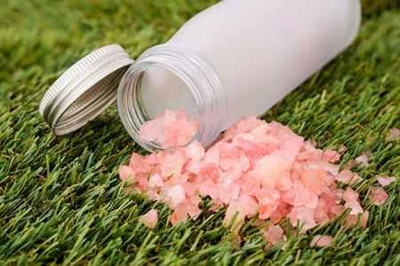Pink sea salt in a white bottle on green grass. Selective focus.の写真素材