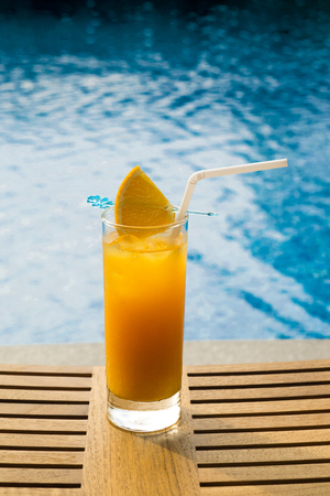 Orange juice in a glass on the wooden table by the pool.の写真素材