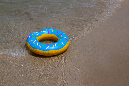 Colorful swimming rings with soft wave of blue ocean in outdoor sun lighting on sandy beach....