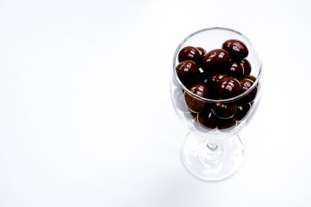 Sweets that are coated with chocolate in a clear glass cup. Colorful candies background top view. White background with text areaの写真素材