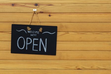 Welcome poster hung on a chalkboard hanging outside. Open Sign On Wood Doorの写真素材