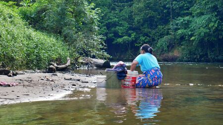 A woman is doing her laundry on the riverbank at Gunung Mulu Nationalpark, Borneoの写真素材