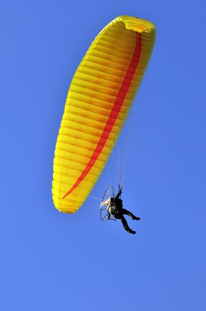 Man with a yellow paraglider flying in the skyの写真素材