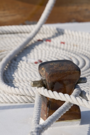 Detail of a sailboat deck with two ropes tied up on a bitt and one rolled rope の写真素材