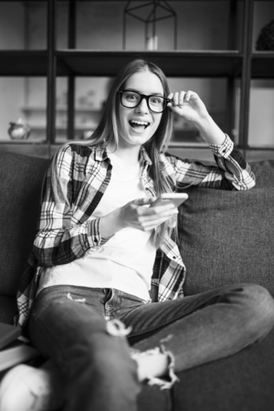 Portrait of a cute girl in glasses with phone on the sofa. Black and whiteの写真素材