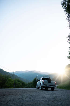 Pickup truck in the background of mountains with a sun glare. Beautiful car is driving along the road in the forestの写真素材