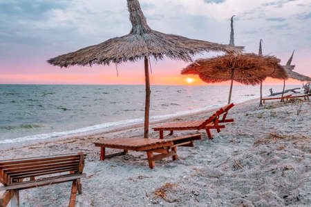 Sunrise on the beach. Sun loungers and straw umbrellas, in the rays of the rising sun. Beach without people.の写真素材