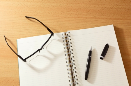 Notebook with pen and glasses on wooden tableの写真素材