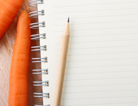 Directly above close-up view of a table with a Carrots and a notebook on cutting boardの写真素材