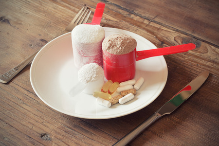 Whey protein powder in scoop with vitamins on plate on wooden backgroundの写真素材