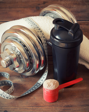 Whey protein powder in scoop with  plastic shaker on wooden backgroundの写真素材