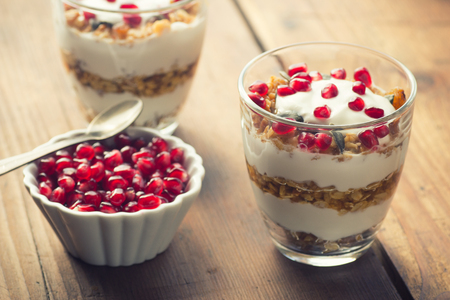 yogurt with homemade granola and pomegranate on the bright wooden boardの写真素材