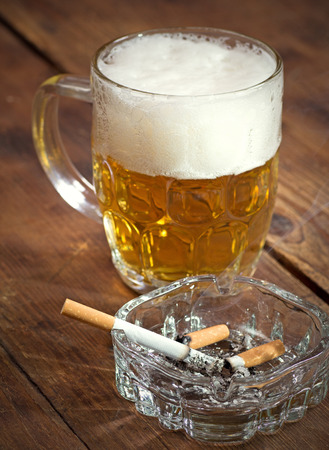 Burning cigarette in a glass ashtray and mug of beerの写真素材