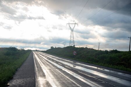 The highway wet with freshly fallen rainwater, and in the background a power transmission tower and a traffic sign. On the horizon the blue sky amid cloudsの写真素材