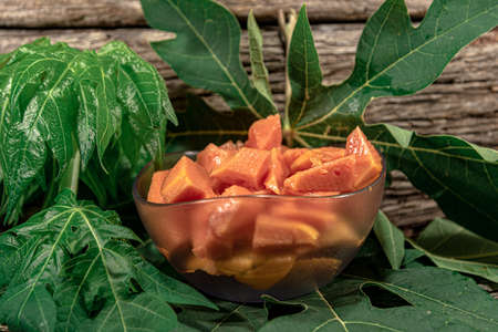 Bowl with pieces of papaya. Tropical fruit. Edible fruit with digestive properties. Green leaves. Wood background. Fruit for juices. Natural food and detox.の写真素材