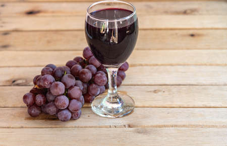 Bunch of pink grape and glass of natural juice. Wood background. Table grapes ready for consumption. Crystal with grape juice. Fruit for making juices and jams. Vine product. Detox berries.の写真素材