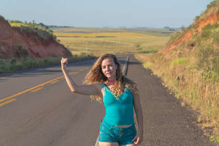 Brazilian woman wearing a hat showing a planting field. Girl pointing a field of soy cultivation. Rural lifestyle. Peaceful landscape. Blonde and young woman in farm area.の写真素材
