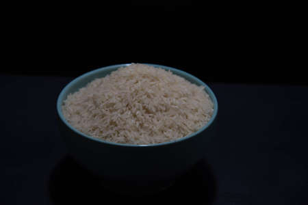Porcelain pan with raw white rice on black background. White rice. Human food. Cereals rich in starch and source of nutrients. Culinary delicacy.の写真素材