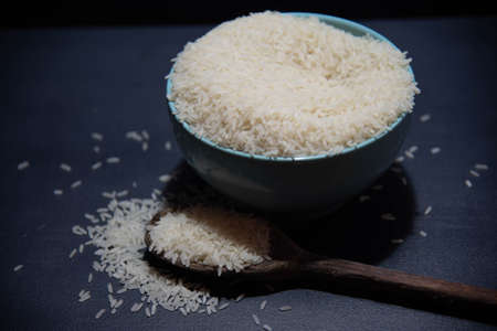 Raw rice served in porcelain frying pan and wooden spoon on dark background. Human food product. Natural food. Scattered cereal grains.の写真素材