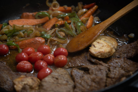 Steak with onions and red tomatoes being prepared in a residential kitchen..の写真素材