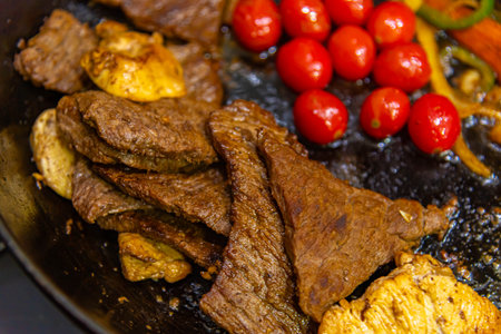 steak with onions, tomatoes and peppers being prepared in a frying pan on a gas stoveの写真素材