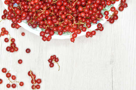 Fresh red currant berries pouring out of white bowl on wooden tableの写真素材