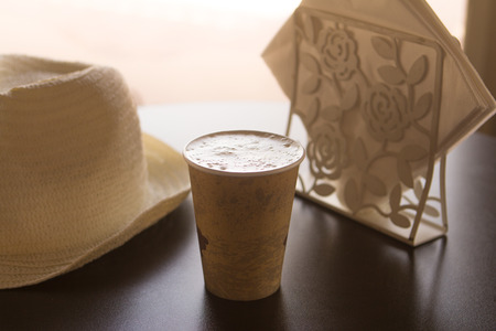 A cup of coffee on a table in a cafe with a white hat and white napkinsの写真素材