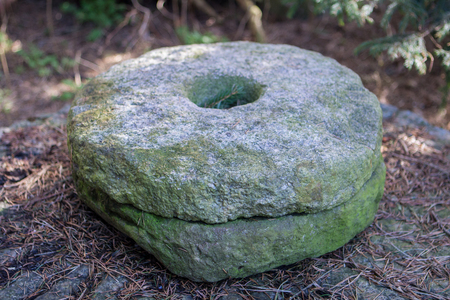 old stone hand-made millstones for grinding grain in a village in green moss in a pine forest as a symbol of antiquity and the pastの写真素材